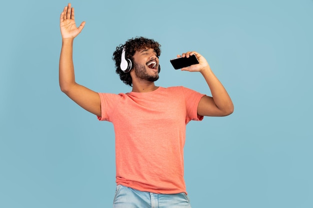 Joyful indian guy singing karaoke using smartphone and headset