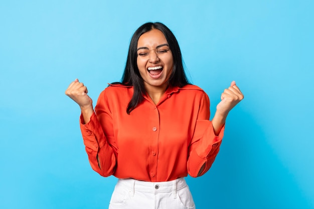 Joyful indian lady shaking fists shouting in joy blue background