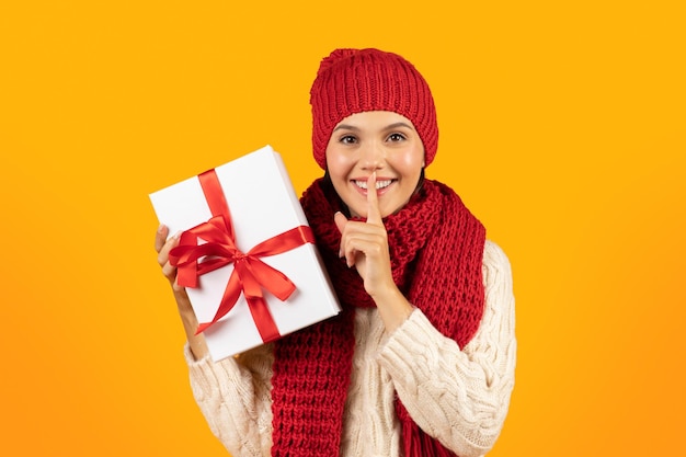 Joyful lady holding holiday wrapped present gesturing hush sign studio