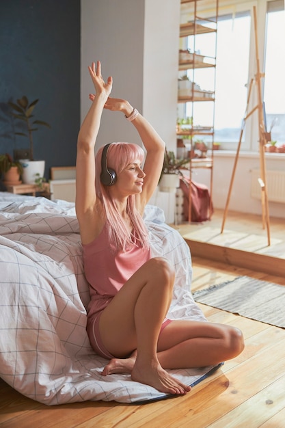 Радостная дама с поднятыми руками слушает музыку в наушниках, сидя на полу