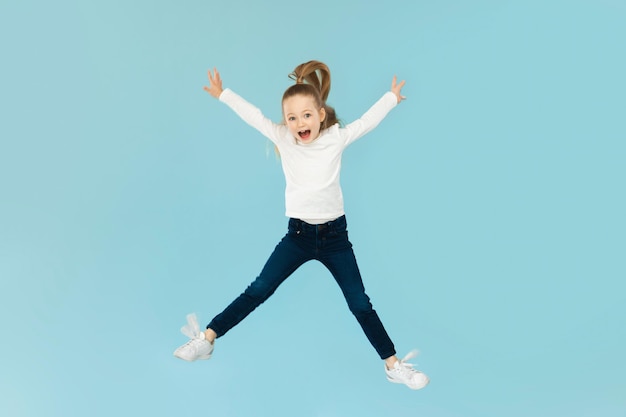 Joyful little girl jumping having fun posing blue background