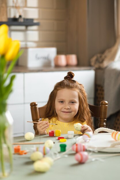 Joyful little girl paints eggs for Easter holidays Happy Easter