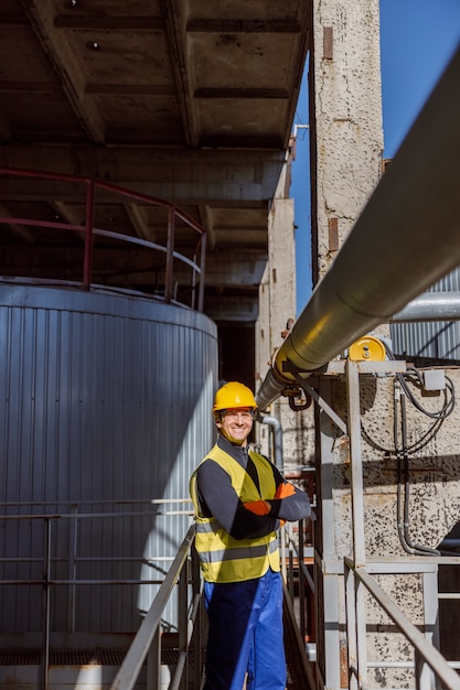 Joyful male engineer standing near metal pipe at factory