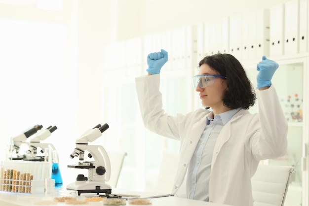 Joyful male scientist in protective goggles raises hands