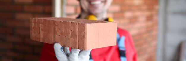 Joyful male wearing yellow helmet hold brick