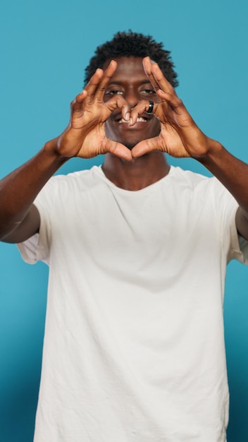 Joyful man doing heart shape symbol with hands while looking at camera. Romantic person showing love sign for valentines day. Adult celebrating romance with affectionate gesture.