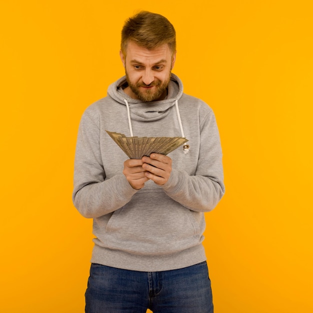 Joyful man in a gray hoodie looks at money dollars on a yellow background image