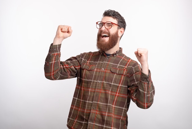 Joyful man is making the winner gesture on white background.