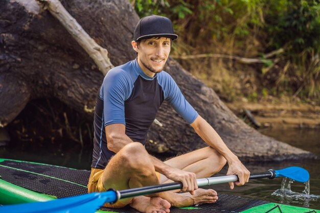 Photo joyful man is training sup board in river on a sunny morning stand up paddle boarding awesome active outdoor recreation