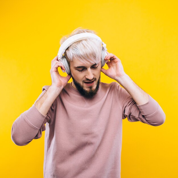 Joyful man listening to music on headphones on a yellow background
