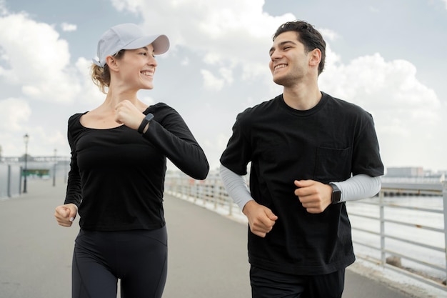 Joyful man and woman in sportswear running together on a sunny waterfront promenade