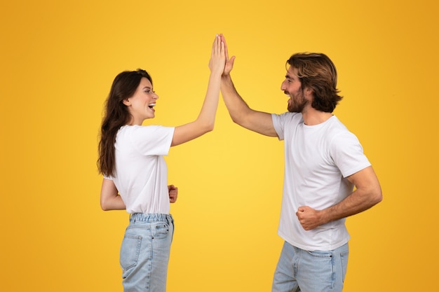 Joyful man and woman in white shirts highfiving showcasing teamwork and excitement