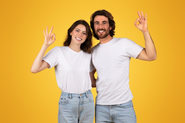 Joyful man and woman in white tshirts and jeans making the ok hand gesture