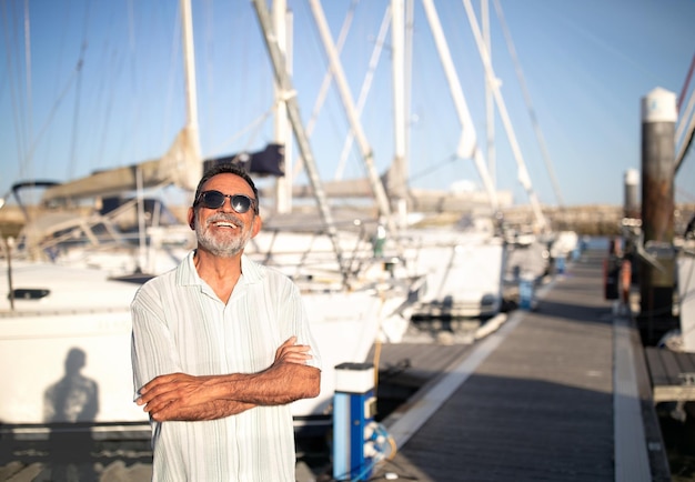 Joyful mature man posing near yachts at marina pier outdoor