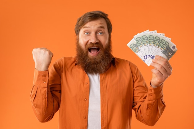 Photo joyful mature redhaired businessman celebrates victory holding euro cash studio