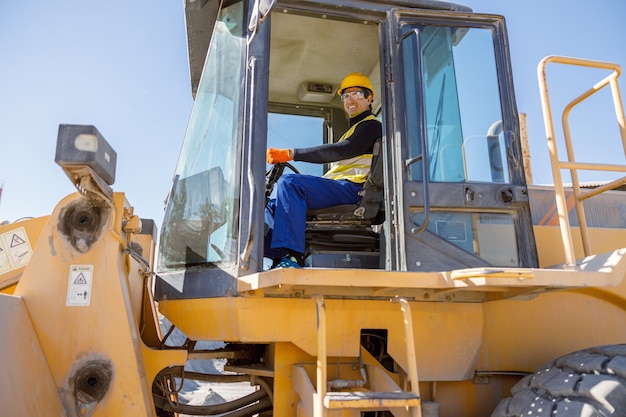 Joyful matured man sitting in tractor at factory