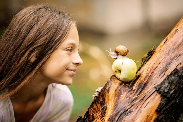 Joyful meeting of a little girl and a snail. Summer photo in the rain.