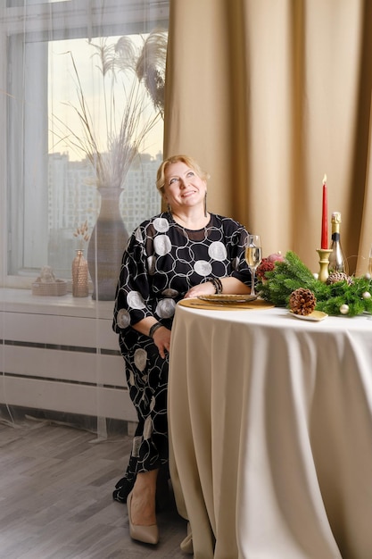 Joyful middle age woman celebrating christmas sitting behind the festive table