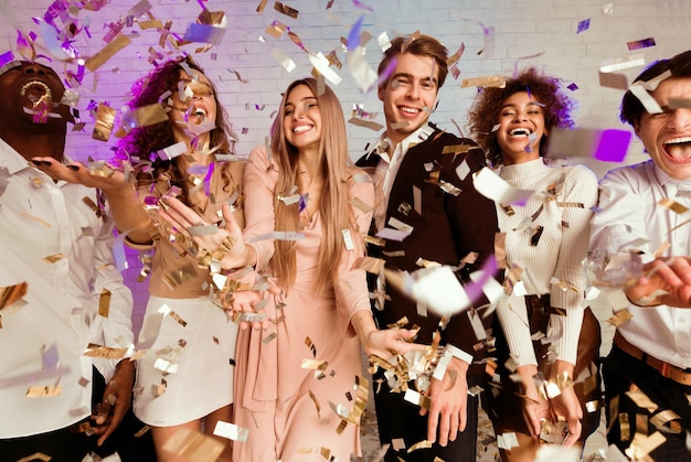 joyful millennial people dancing under falling confetti on party indoor
