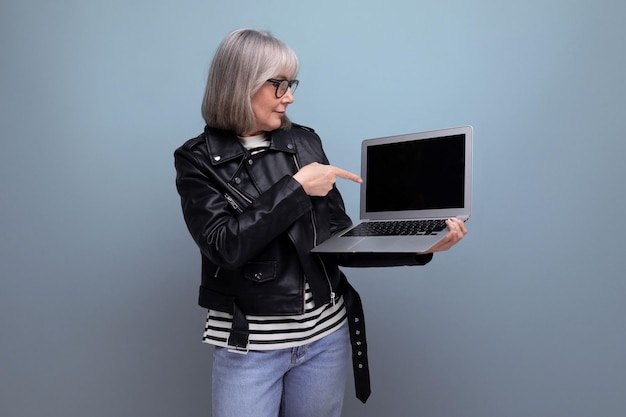 회색 머리를 가진 즐거운 현대 중년 여성 프리랜서가 노트북을 사용하여 인터넷을 서핑합니다.