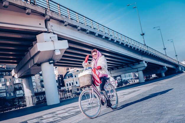 Joyful mood. Beautiful international female keeping smile on her face while riding bicycle