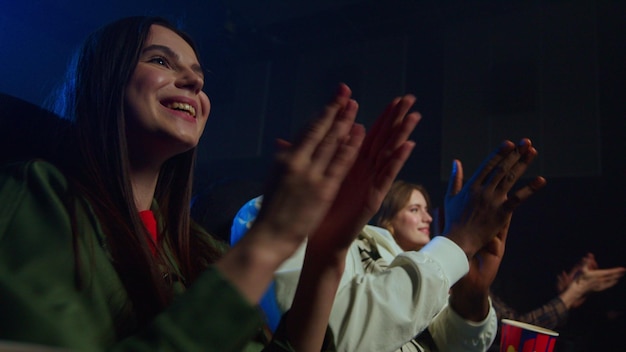 Joyful multicultural people having fun in cinema Cheerful friends applauding in movie theater Smiling multi ethnic people looking to each other in dark hall