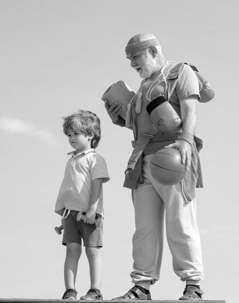 Joyful oldaged man and cute little boy practicing sport and healthy lifestyle over sky background re