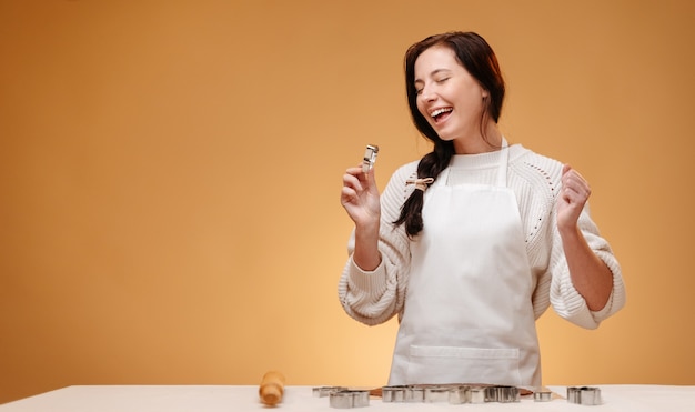 Joyful pastry chef woman in a white apron prepares gingerbread cookies for the holiday christmas