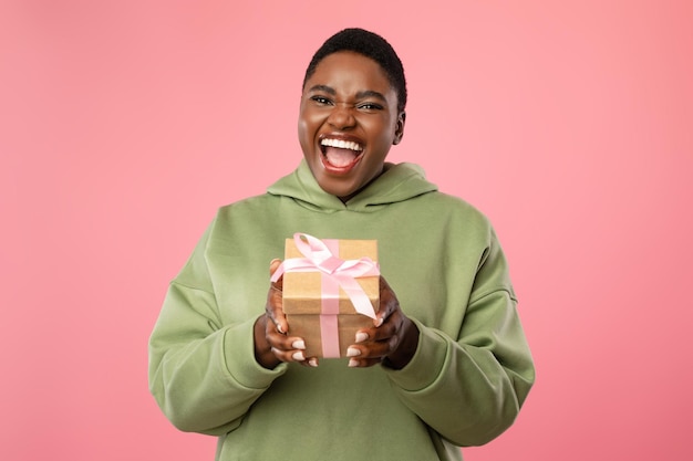 Joyful Plump African American Female Holding Gift Over Pink Background