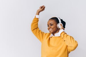 Photo joyful positive young african american woman wears stereo wireless headphones listens audio track and dance people happy emotions and leisure concept