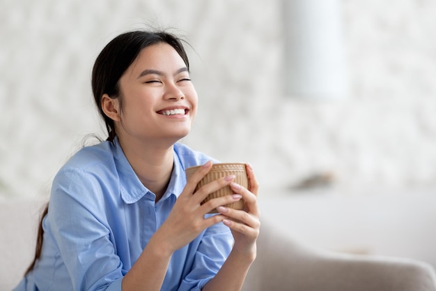 家でコーヒーを飲むうれしそうなかわいいアジアの女性