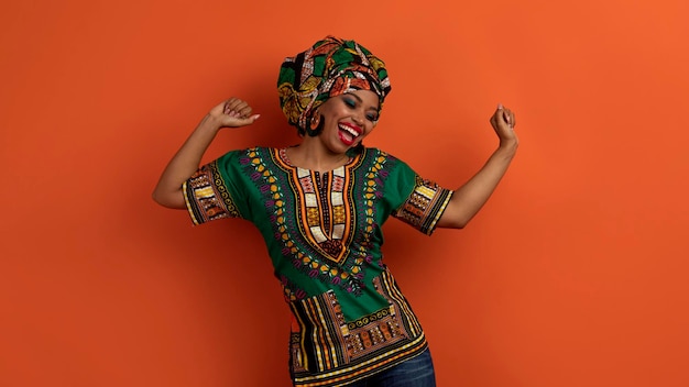 Joyful pretty black woman in african costume dancing on orange