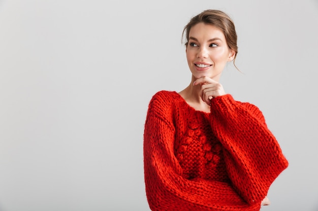 joyful pretty woman in red sweater smiling and looking aside isolated over white background