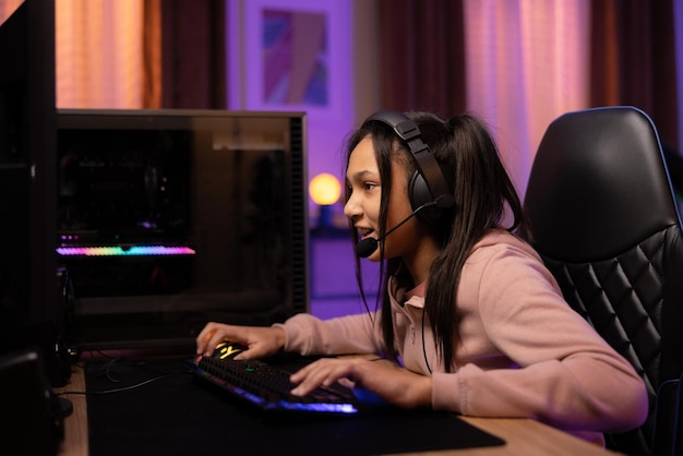 Joyful professional gamer girl wearing headphones with microphone playing online video game