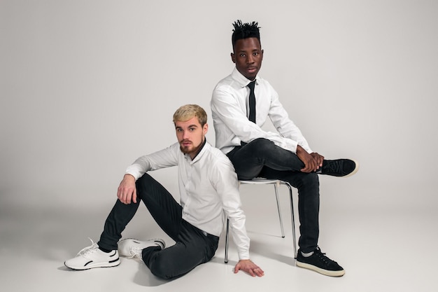 Joyful relaxed african and caucasian boys in white and black office clothes laughing and posing at w...