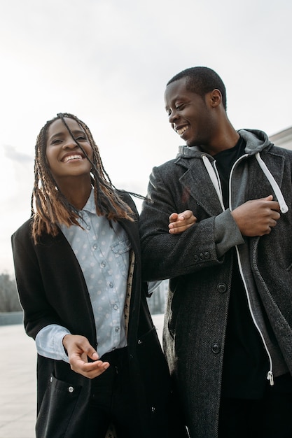 Joyful romantic date. Happy black couple outdoor. African American pedestrians laughing, sky background, street fashion style, happiness concept