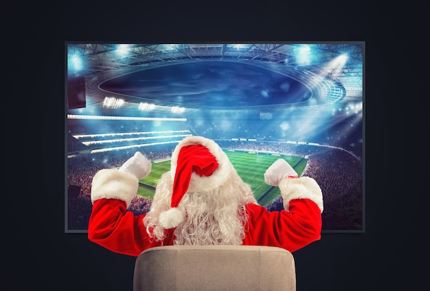 Photo joyful santa claus soccer fan watches a game on television