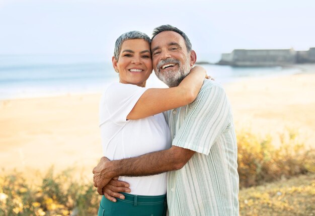 Joyful senior couple hugging standing at stunning ocean view outdoors