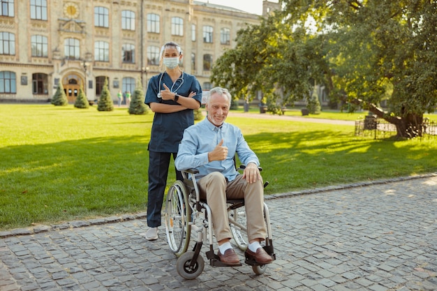 Joyful senior man recovering patient in a wheelchair smiling at camera showing thumbs up together