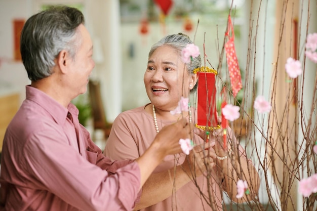 Joyful senior man and woman decorating peach branches for tet celebration