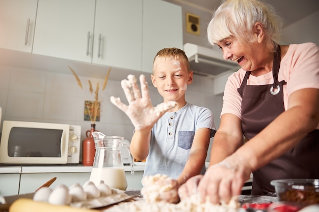 Joyful senior woman and her grandson preparing dough