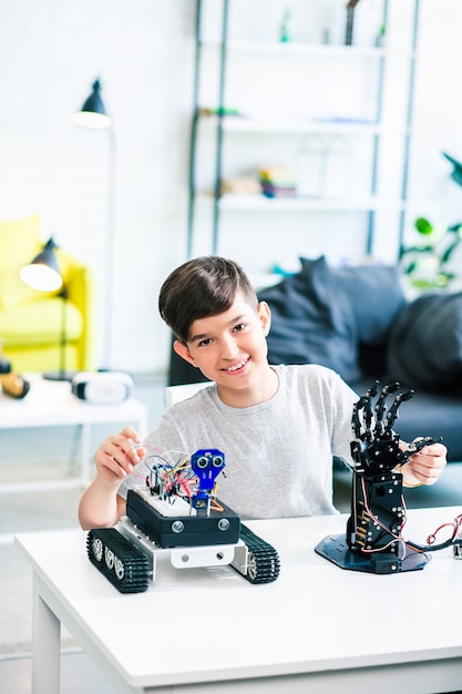 Foto gioioso ragazzino intelligente che sorride e testa le sue creazioni robotiche a casa
