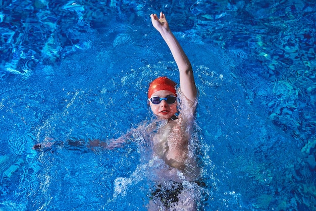 Joyful smiling boy swimmer in a cap and Goggles learns professional swimming in the swimming pool in gym close up