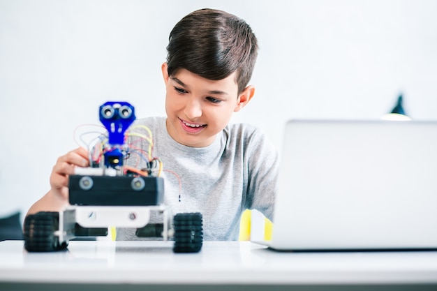joyful smiling boy trying up robot while preparing for engineering classes at home