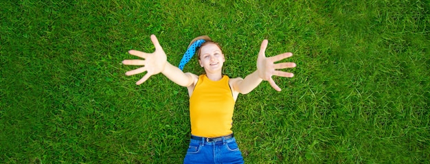 Радостная и улыбающаяся девушка лежит на траве, смотрит в камеру на улице в парке