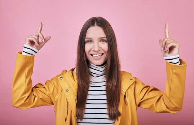 Joyful smiling girl with raincoat and striped golf shows with both fingers up