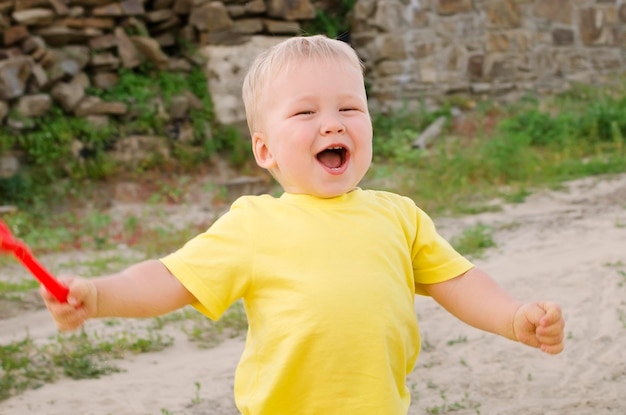 楽しい笑顔の小さな男の子の幼児は、黄色のTシャツで夏の外で遊ぶ肖像画のクローズアップ