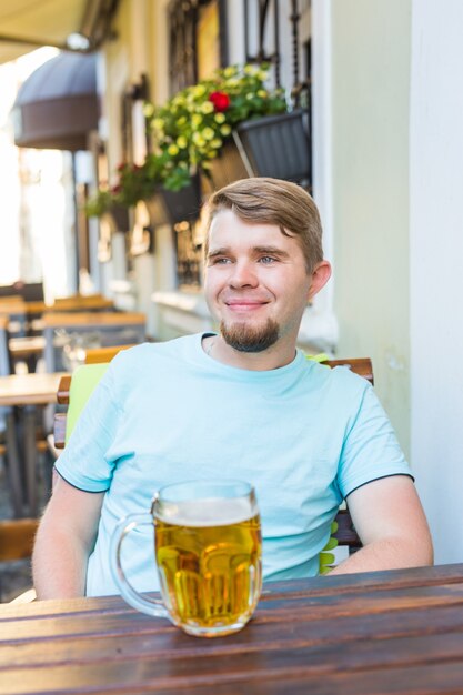 Uomo sorridente allegro che tiene un grande boccale di birra all'aperto