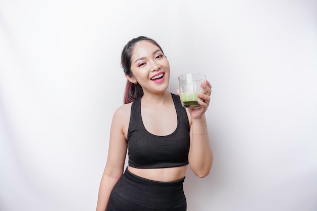 Joyful sporty Asian woman wearing sportswear with glass of tasty green smoothie isolated on white background