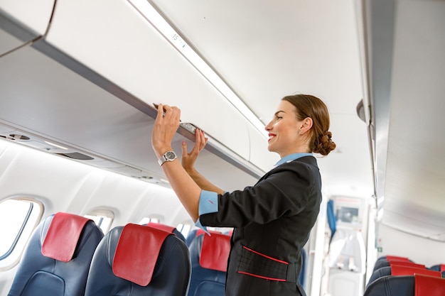 Joyful stewardess closing overhead luggage bin in airplane